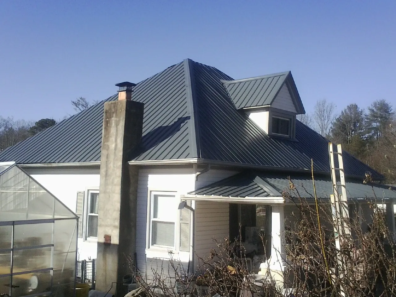 Dark blue standing seam metal roof on a white farmhouse with dormer — Slate & Tile Roof Repair by Roofing Brothers in Elm City