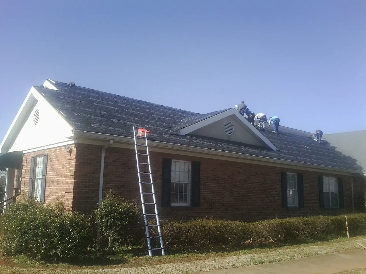 Crew tearing shingles off a brick ranch roof with a ladder set — Emergency Roof Repair work by our crew in Elm City