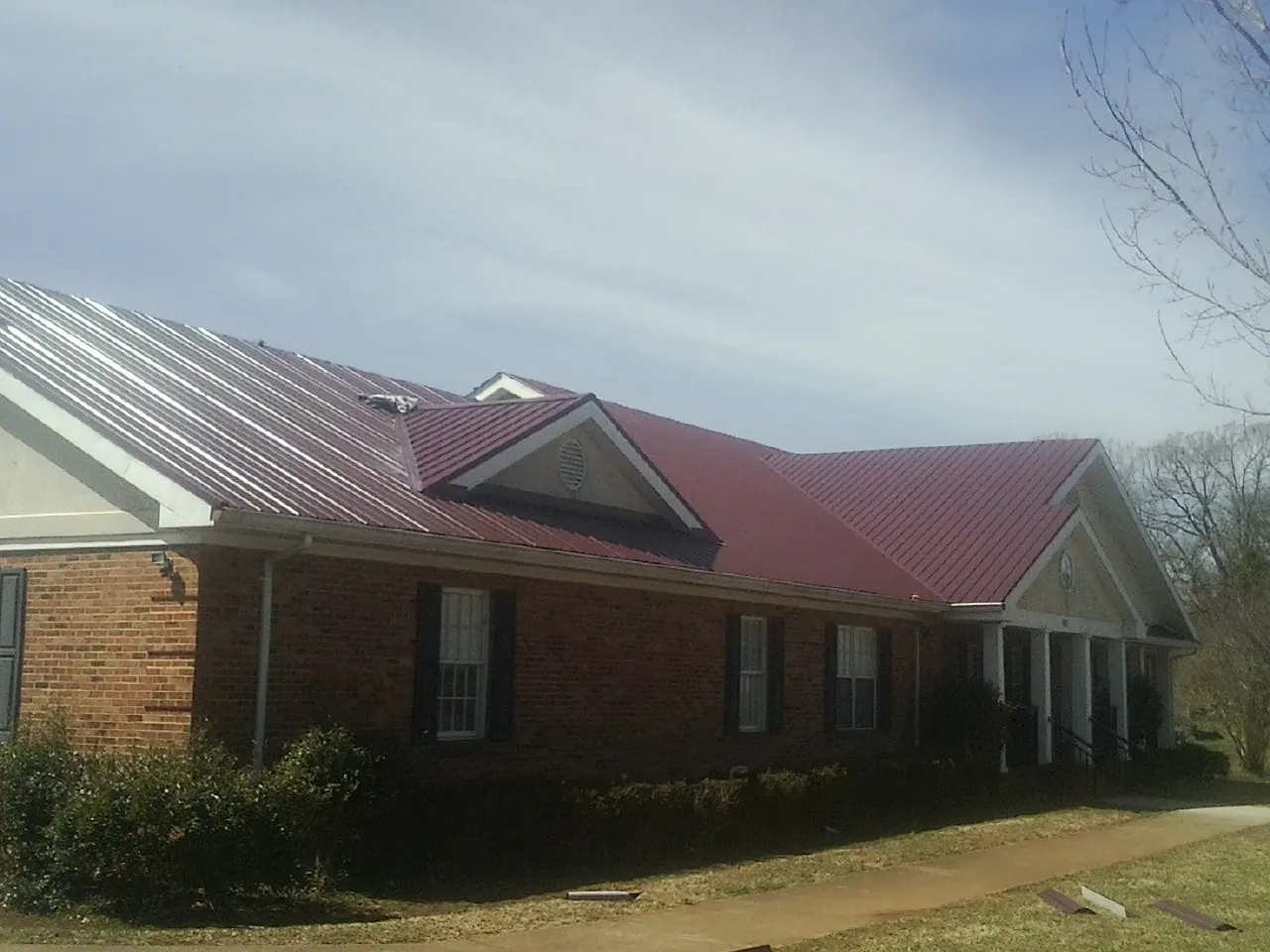 Red metal roof with gabled entries on a long brick building, from a Hail Damage Roof Repair job in Elm City