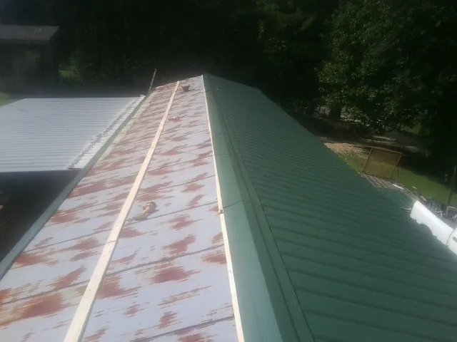 Old rusted panels beside newly installed green metal roofing — Wind Damage Roof Repair by Roofing Brothers in Elm City