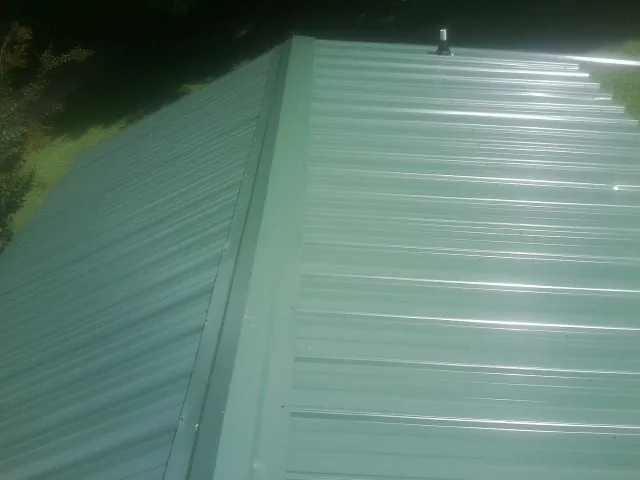 New green metal panels meeting at the ridge of a roof — Flat Roof Repair work by our crew in Elm City