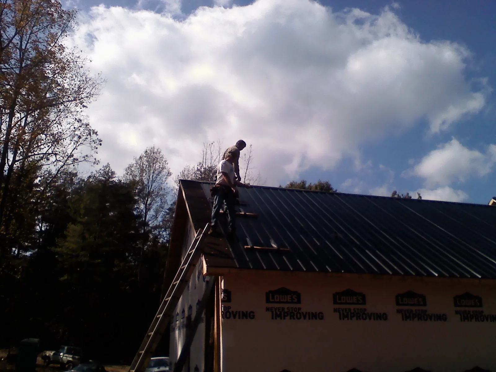 Roofer fastening dark metal panels high against a cloudy sky, from a Roof Inspection job in Elm City