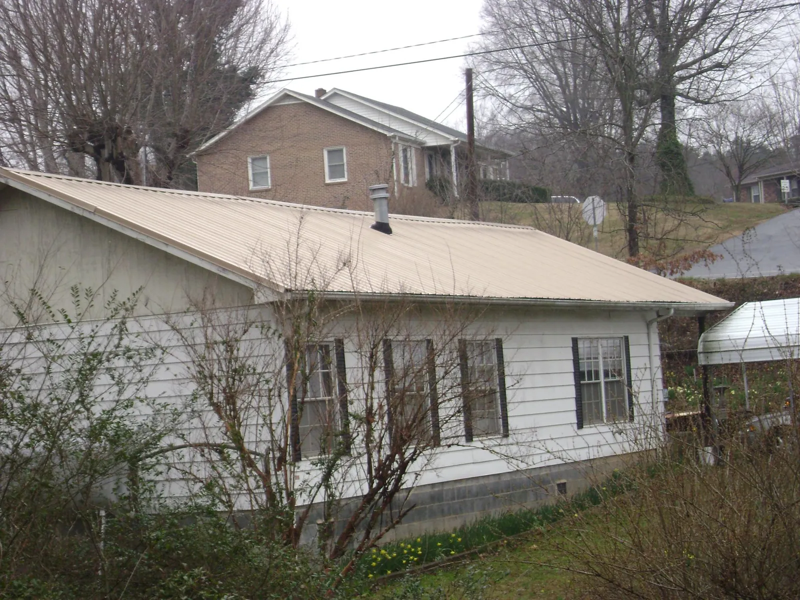 Tan metal roof on a white sided house set into a hillside — Commercial Roofing by Roofing Brothers in Elm City