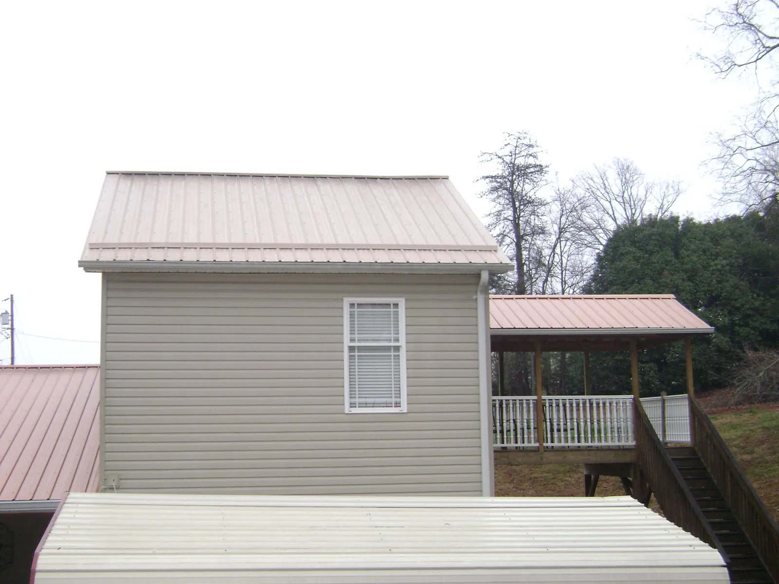 Tan metal roofs on a two story addition and attached porch, from a Roof Replacement job in Elm City